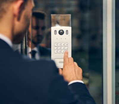 Business professional entering access code on a secure keypad entry system with built-in camera at office building entrance.